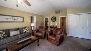 Un salon comprenant un canapé, deux fauteuils en cuir, une table basse, un ventilateur de plafond, une horloge et une armoire.