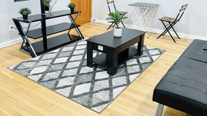 Ein modernes Wohnzimmer mit einem Flachbildfernseher, einer Holztür, einem kleinen Tisch mit Stühlen und einem schwarzen Sofa.