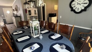 Uma sala de jantar com toalha de mesa azul, cadeiras de madeira, um candelabro e um relógio de parede.