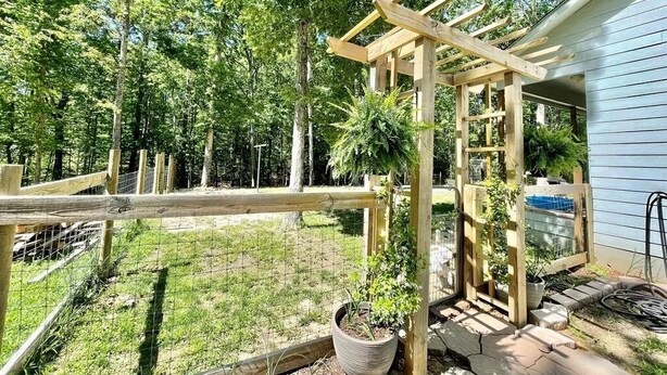 A wooden pergola structure in a backyard with a house in the background.