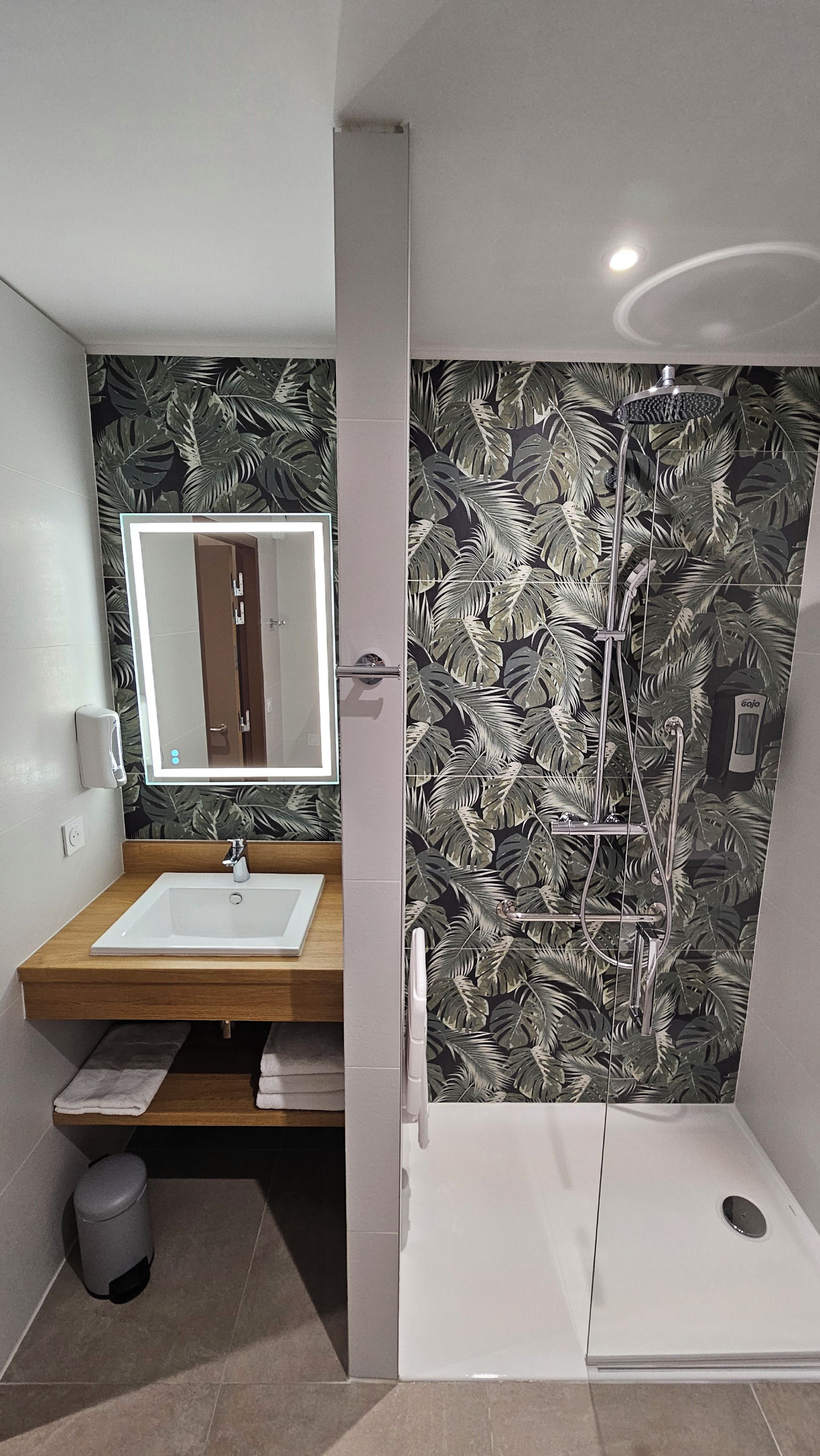 A bathroom with a wooden vanity, a mirror, a shower with a rain showerhead, and a toilet.