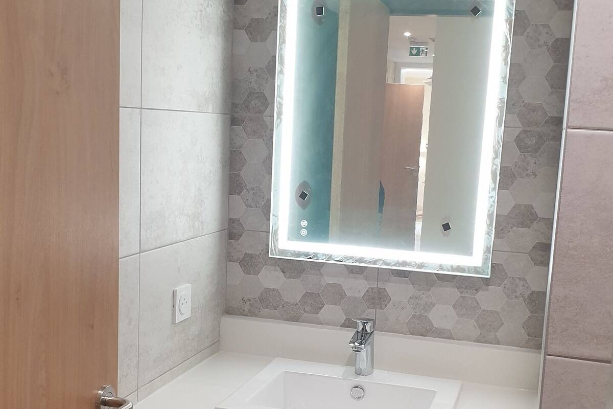 Un baño con lavamanos blanco, un espejo con luz y una puerta de madera.