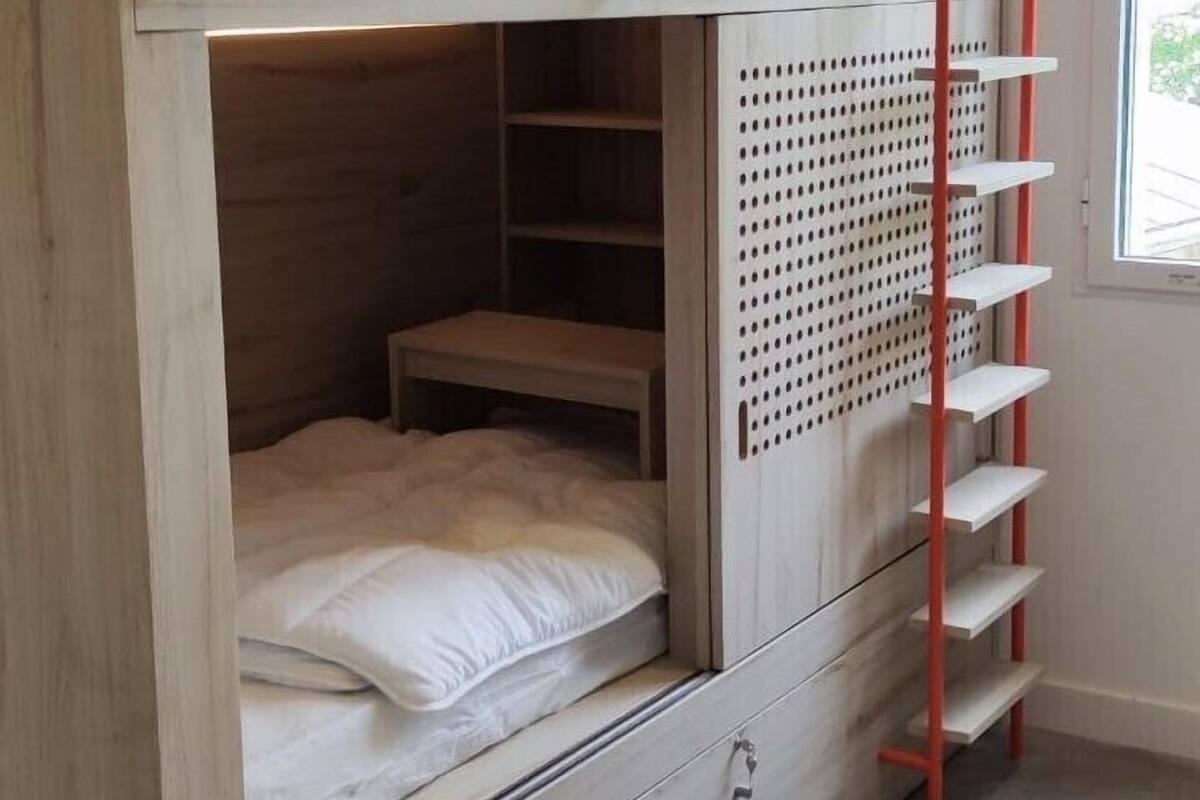 Una cama litera con acabado de madera, una escalera roja y un estante con diseño perforado.