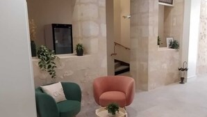 Ein modernes Interieur mit einer Steinwand, einem grünen Sessel, einem pinken Sessel und einem kleinen runden Tisch mit einer Pflanze.