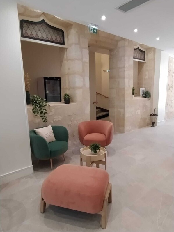 A modern interior with a stone wall, a green armchair, a pink armchair, and a small round table with a plant.
