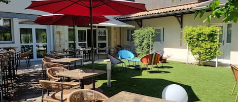 An outdoor patio area with tables and chairs, a red umbrella, and a well-maintained lawn.