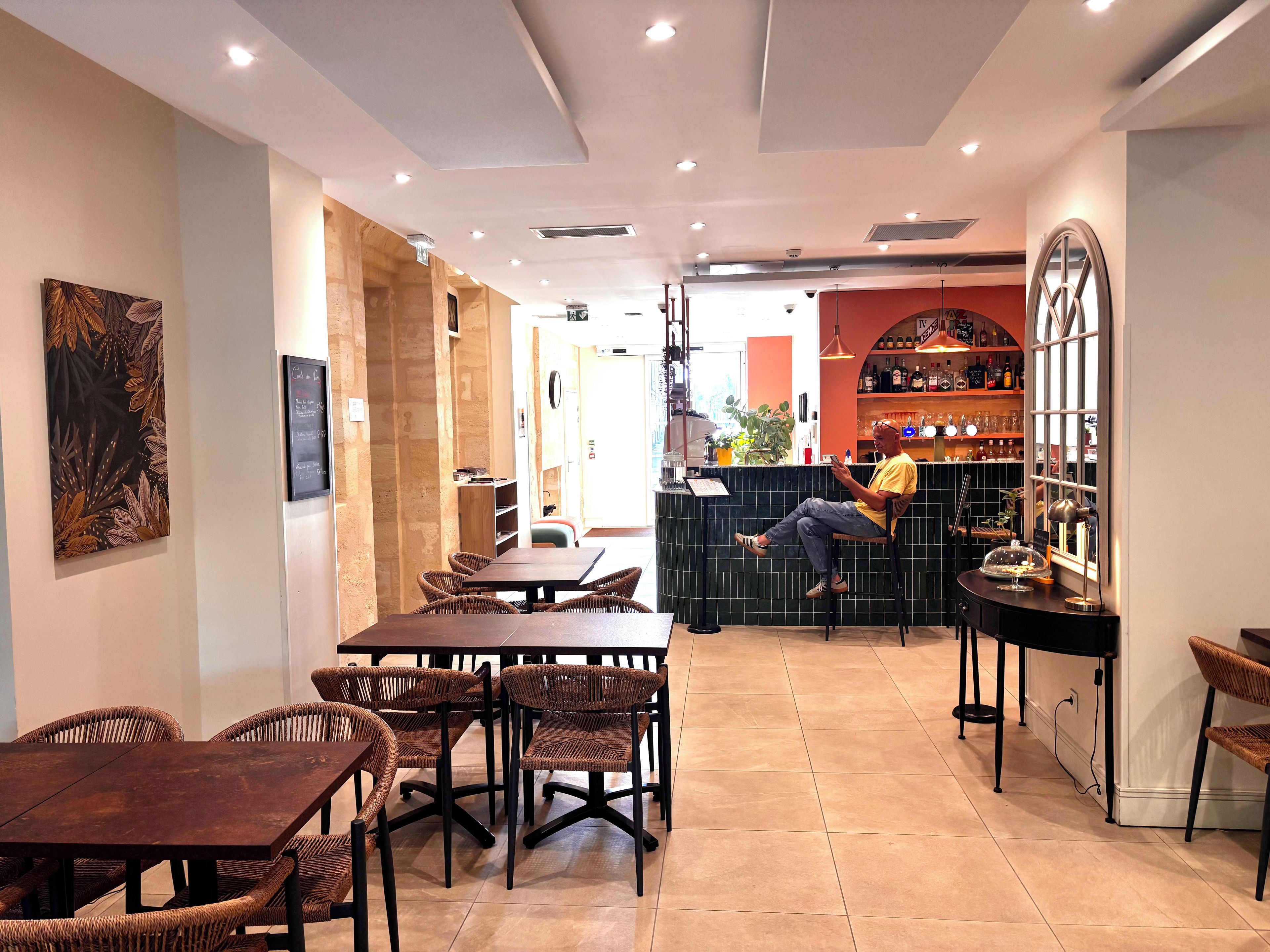 Interior de un restaurante con barra, mobiliario de mimbre y una persona sentada en una mesa.