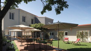 Eine Terrasse mit Gartenmöbeln, Sonnenschirmen und einem gepflegten Rasen.