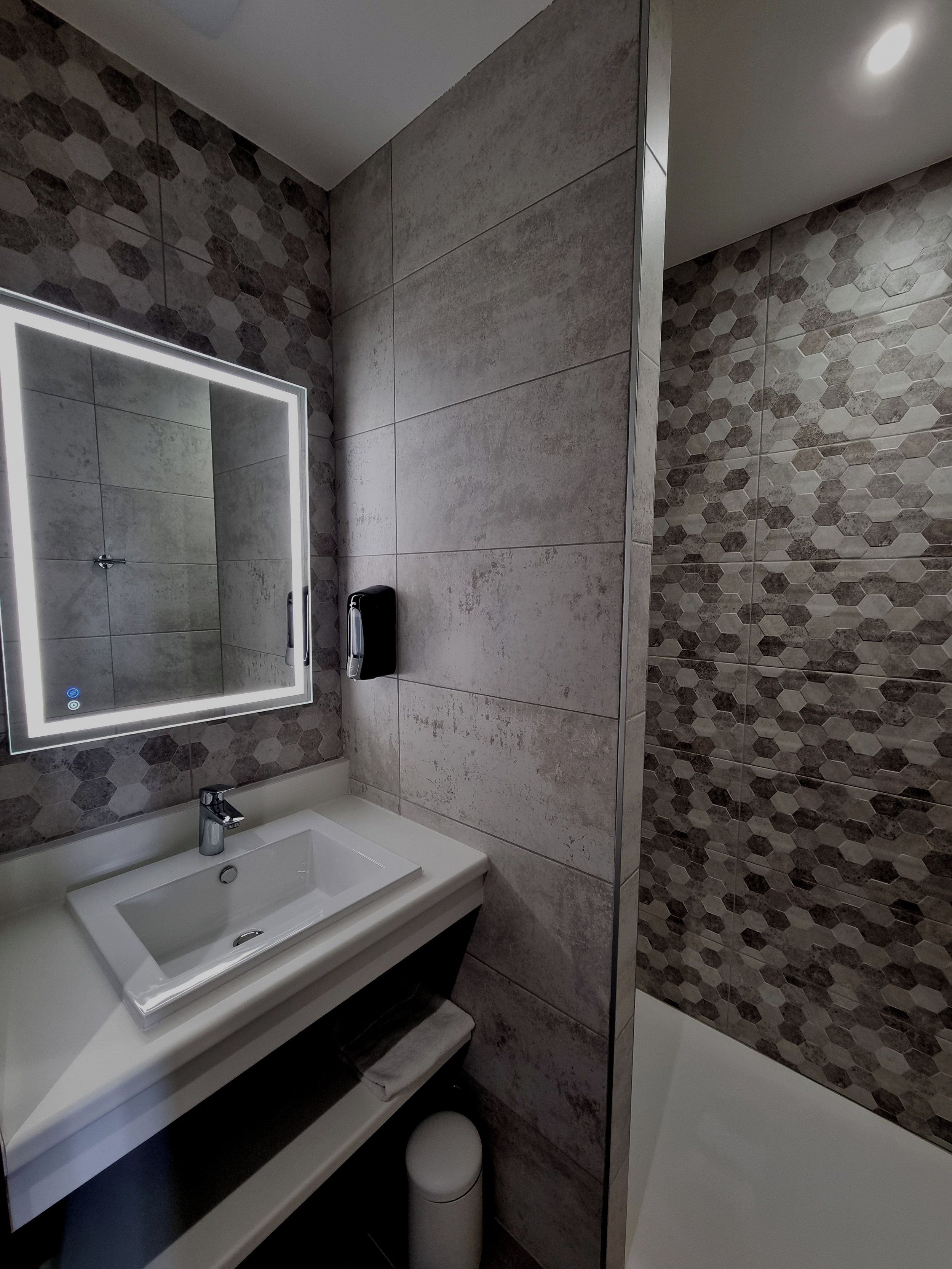 A bathroom with a white sink, a mirror with lights, a towel rack, and hexagonal patterned tiles.