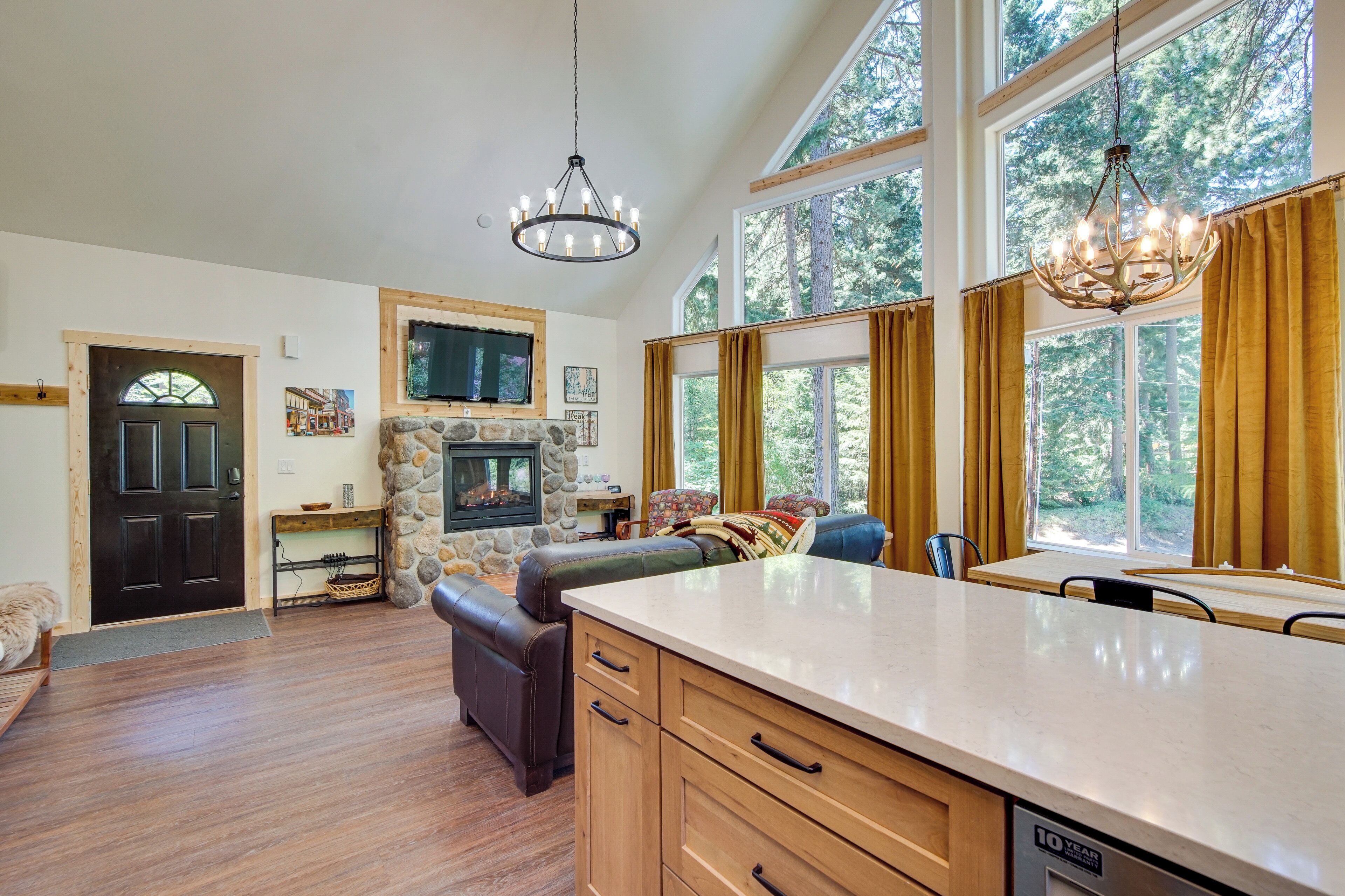 A spacious living area with a stone fireplace, a large window with curtains, and a modern kitchen with a built-in dishwasher.