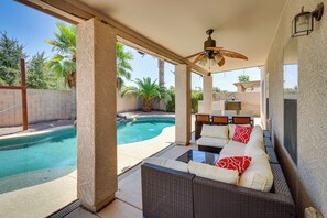 Un espace extérieur abrité, aménagé avec des meubles en osier, un ventilateur de plafond et offrant une vue sur une piscine.