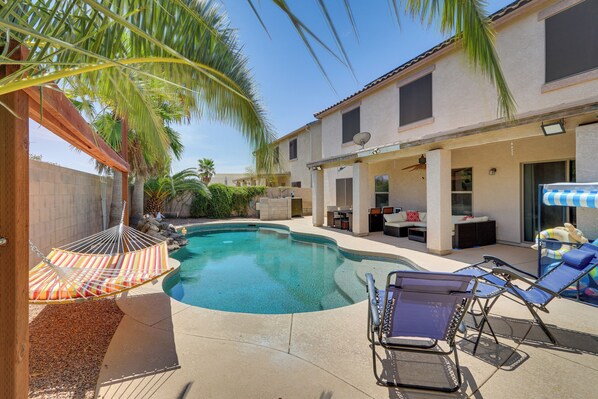 Un jardin avec une piscine, des chaises longues, un hamac et un espace patio aménagé avec du mobilier d’extérieur.