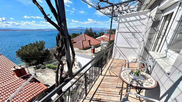 A balcony with a view of the sea, a tiled floor, and a table with a vase.