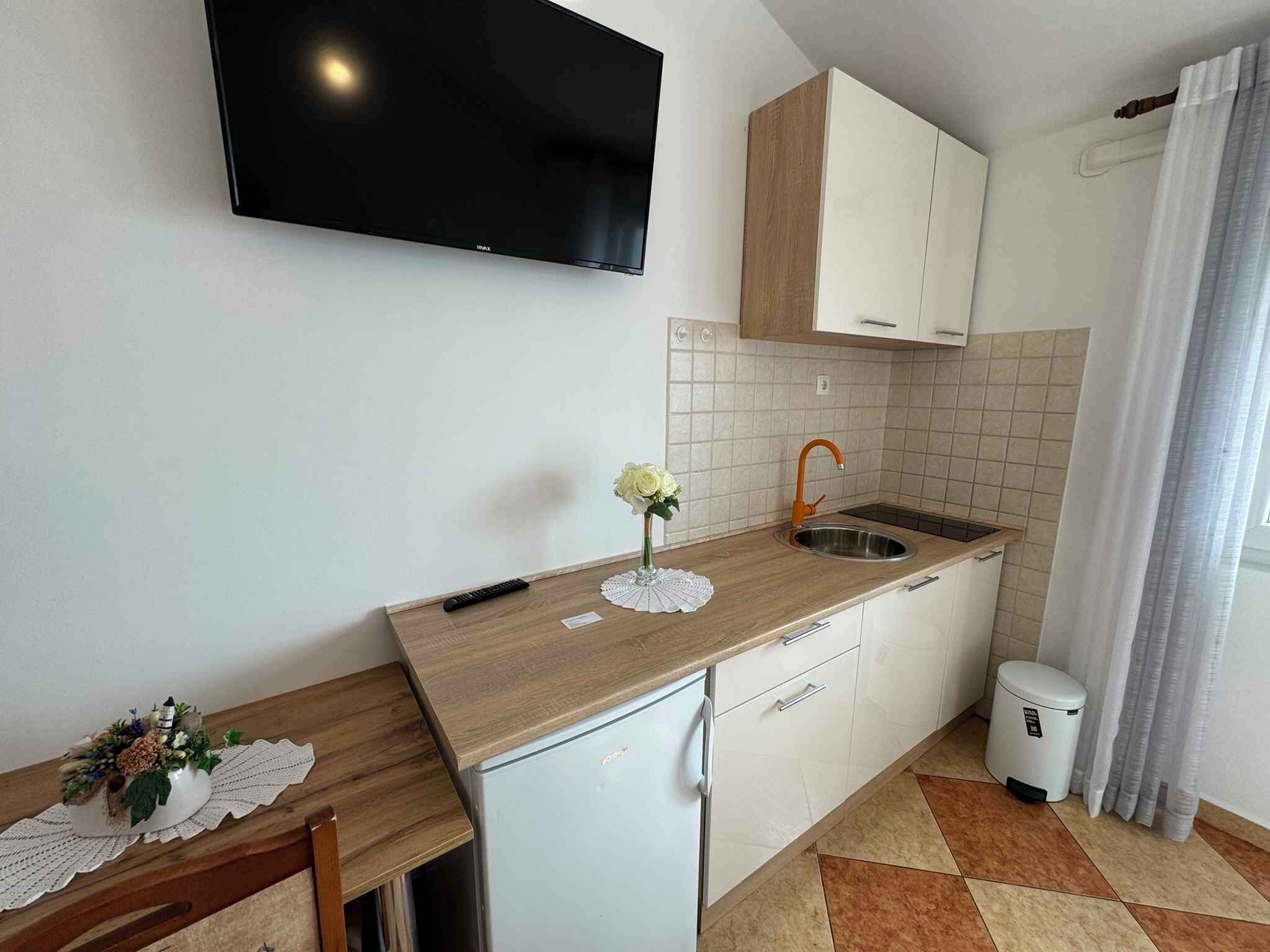 A compact kitchen with a wooden countertop, white cabinets, a built-in sink, and a television mounted above the counter.