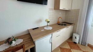 A compact kitchen with a wooden countertop, white cabinets, a built-in sink, and a television mounted above the counter.