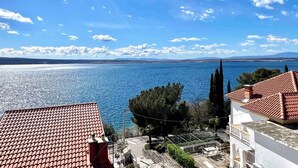 A coastal view with a clear sky, a body of water, and buildings with red-tiled roofs.