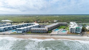 A coastal hotel with multiple buildings, a swimming pool, and a beach view.