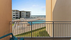 A balcony with a view of a swimming pool, beach, and adjacent buildings.