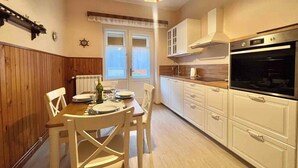 A compact kitchen with white cabinets, a built-in oven, and a dining area with wooden chairs and a table set for two. - Holiday apartment first row to the sea with balcony (Crikvenica)
