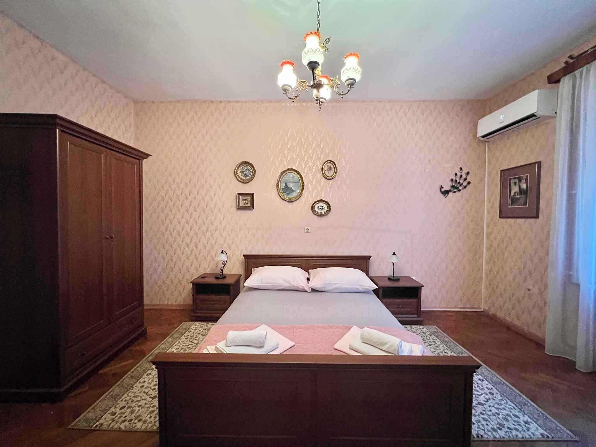 Quarto com cama grande, guarda-roupa de madeira e lustre.