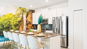 Enjoy cooking in this kitchen with a large island, sink, and stainless steel refrigerator, complemented by white cabinetry and a black tile backsplash.