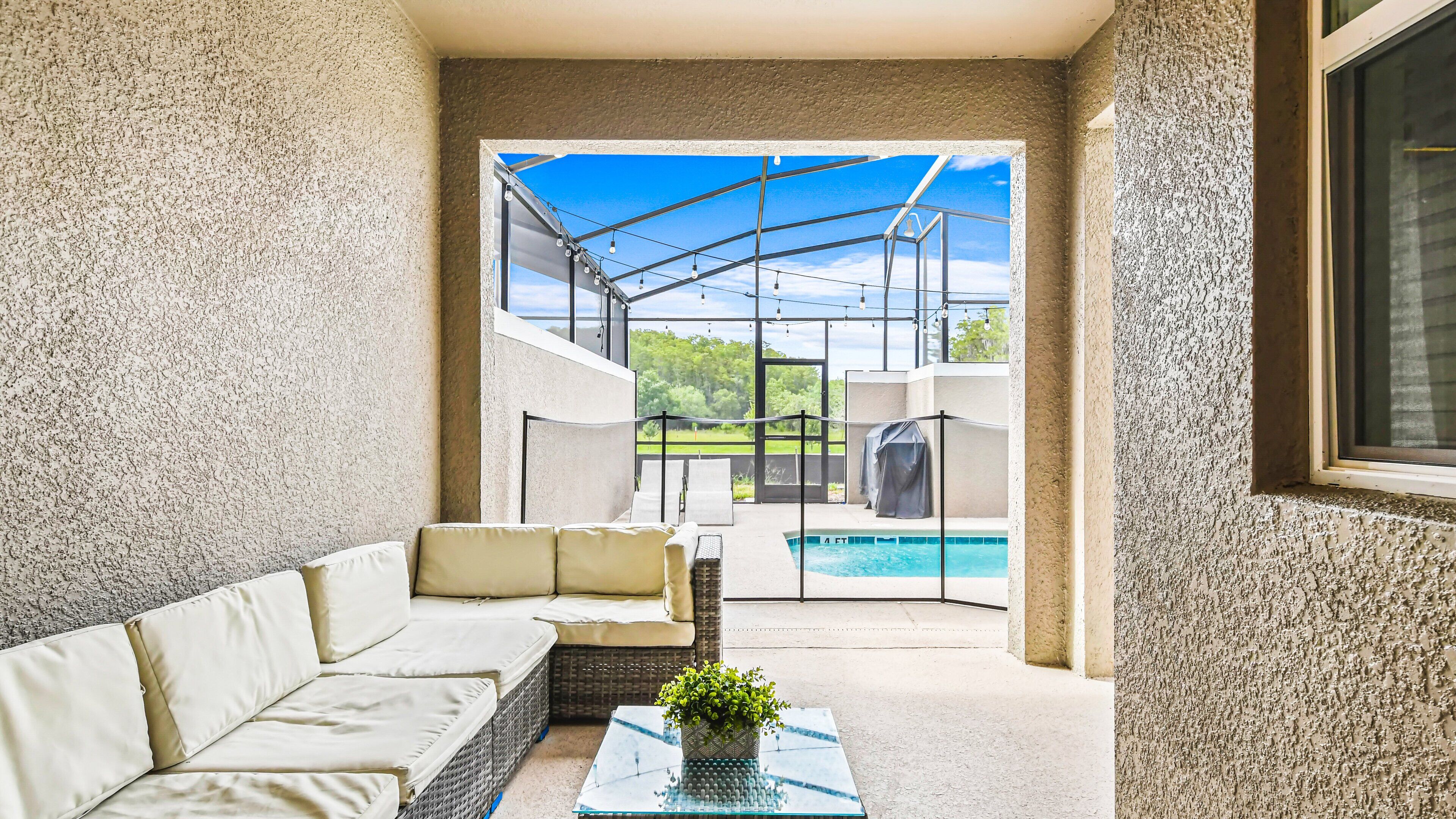 A covered patio with a pool, outdoor seating, and a view of the pool area.