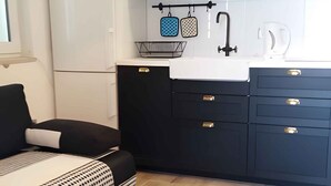 A modern kitchen with dark cabinets, a white refrigerator, and a microwave. There's a sink with a faucet, a black countertop, and a small table with a bowl. - Holiday apartment with sea view and terrace (Orebić)