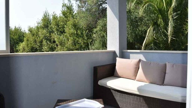 A balcony with a wicker sofa and a small table, overlooking a lush green landscape. - Holiday apartment with sea view and terrace (Orebić)
