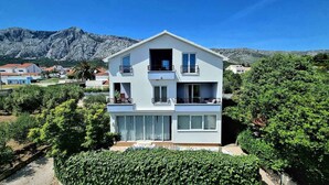 Un immeuble de deux étages doté de balcons, entouré de verdure et avec des montagnes en arrière-plan.