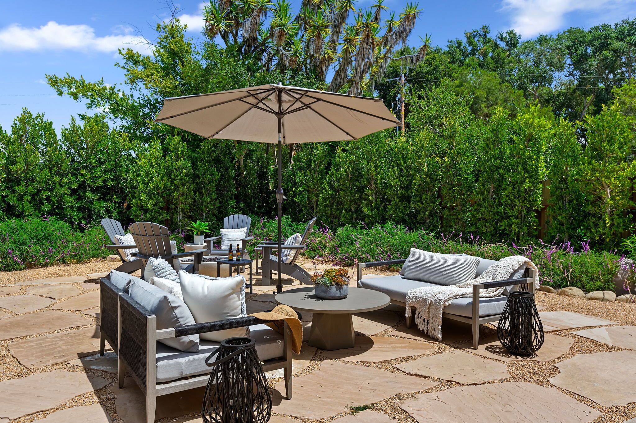 Une terrasse extérieure avec une table ronde, deux canapés et un grand parasol.