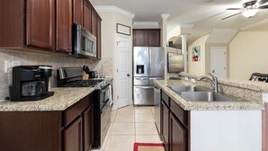 A modern kitchen with dark wood cabinets, stainless steel appliances, granite countertops, and a built-in oven. - Reunion 3BR Townhouse with Private Patio (Kissimmee)