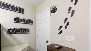 A room with a white door, a white desk, and a wooden dresser. There are three signs on the wall: 'LIGHTS', 'CAMERA', and 'ACTION'. A sign on the wall says 'PLATFORM 9/4'. There are footprints on the wall and a remote control on the dresser. - Reunion 3BR Townhouse with Private Patio (Kissimmee)