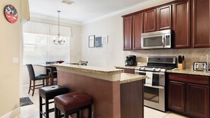 A modern kitchen with dark wood cabinets, stainless steel appliances, a granite countertop, and a bar area with stools. - Reunion 3BR Townhouse with Private Patio (Kissimmee)
