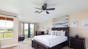 A bedroom with a large bed, a ceiling fan, a view of the outdoors, and a small desk with a lamp. - Reunion 3BR Townhouse with Private Patio (Kissimmee)