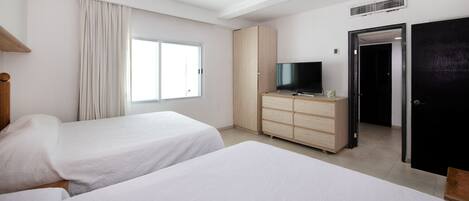 Habitación de hotel con dos camas, un televisor sobre una cómoda de madera, una ventana con cortinas y una puerta.
