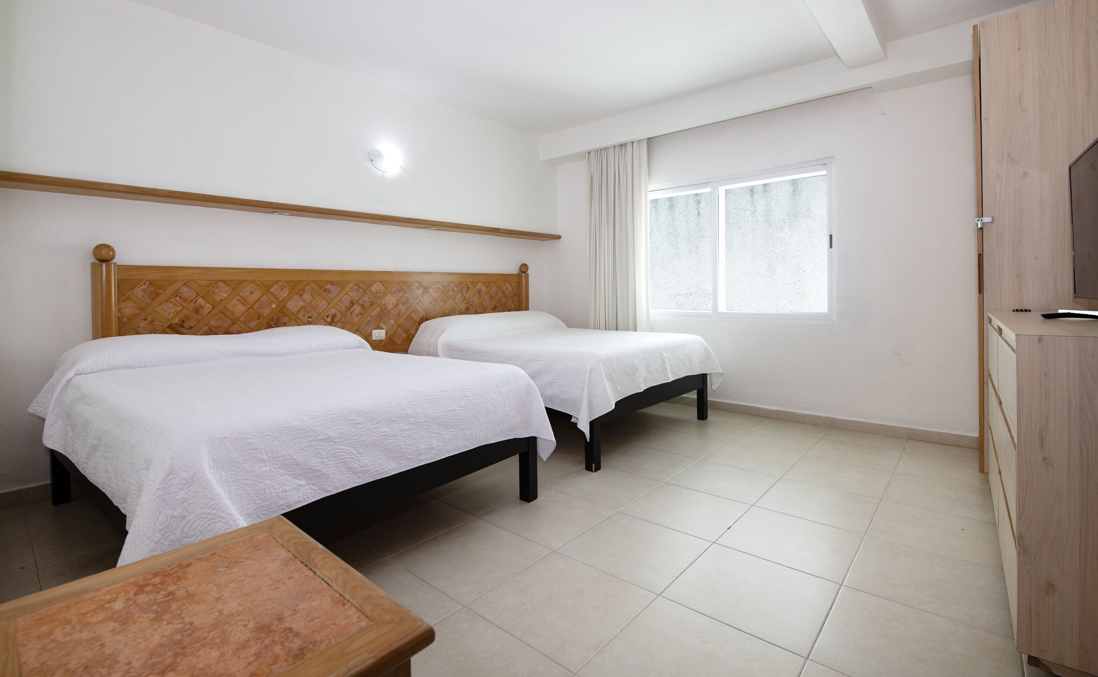 Een hotelkamer met twee bedden, een houten hoofdbord, een raam met gordijnen en een houten kast.