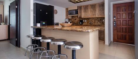 Une cuisine moderne dotée d’un îlot central, de tabourets de bar, de meubles en bois et d’un four encastré.