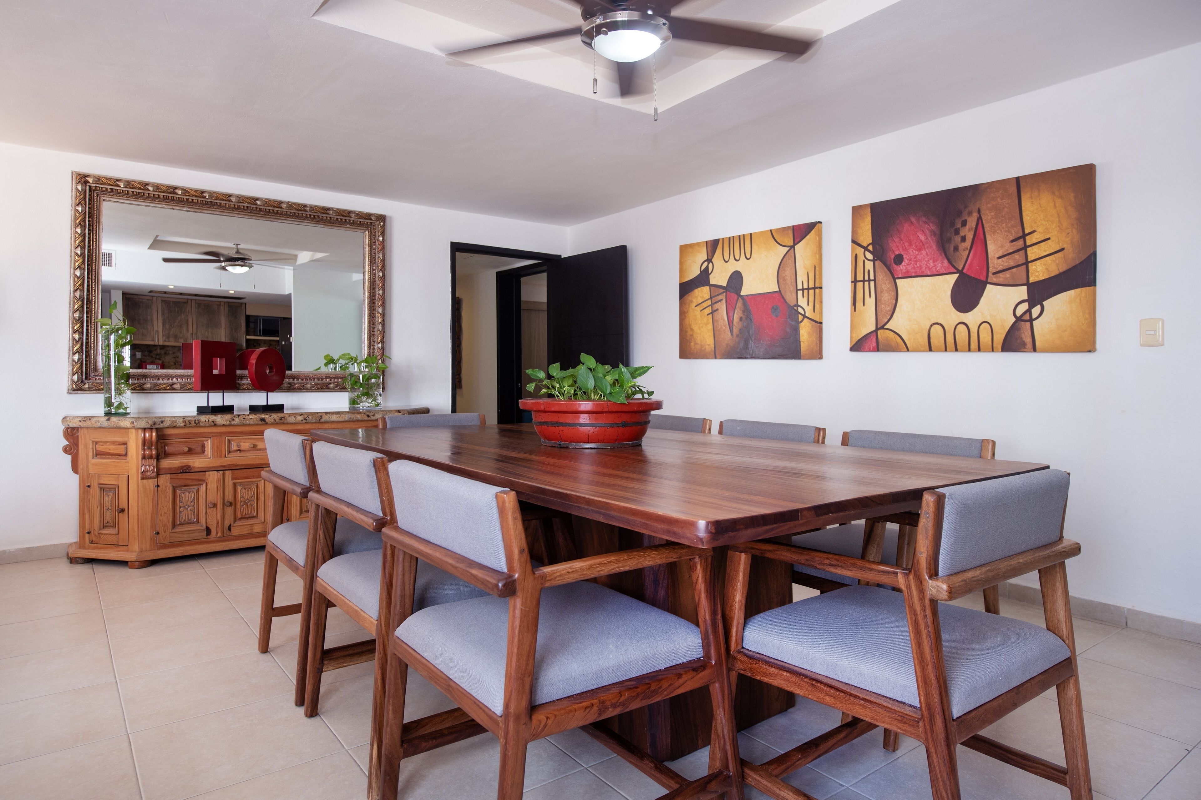 Un coin repas avec une table et des chaises en bois, un grand miroir et des tableaux abstraits accrochés au mur.