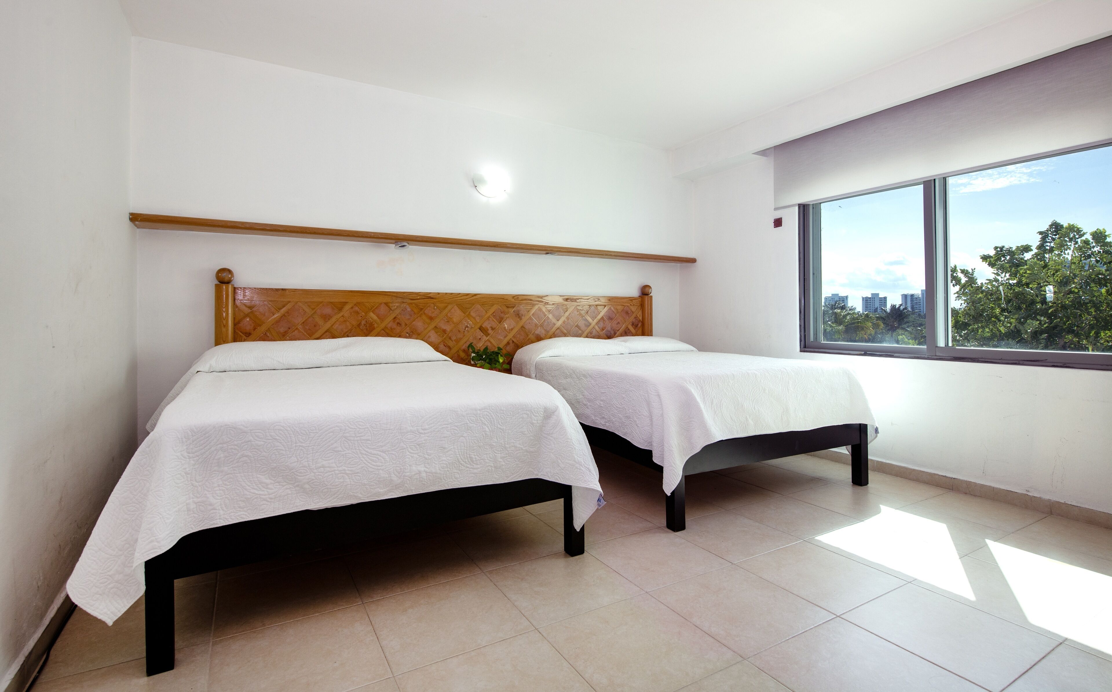 A room with two beds, a wooden headboard, a large window, and a view of buildings and trees.