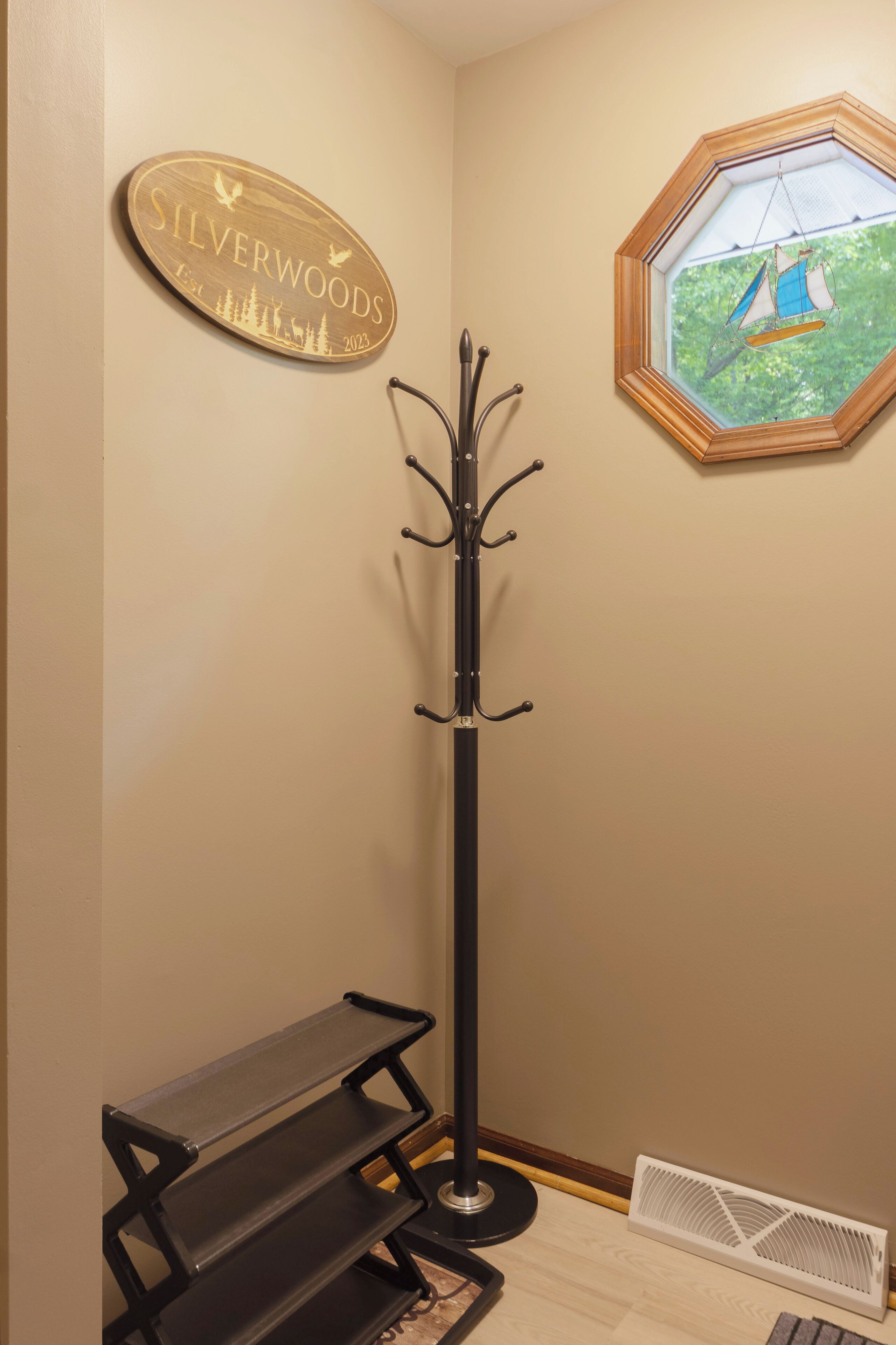 Un coin de pièce avec un porte-manteau, un banc, une enseigne indiquant « Silverwoods », et un tableau encadré représentant un voilier.