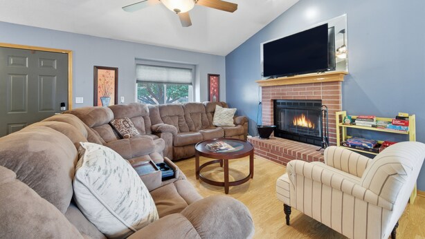 Una sala de estar con un sofá seccional, un sillón reclinable, una chimenea y un televisor de pantalla plana montado encima.
