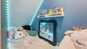 Una habitación acogedora con cama, peluches, un cuadro enmarcado y un estante con libros y un animal de peluche.