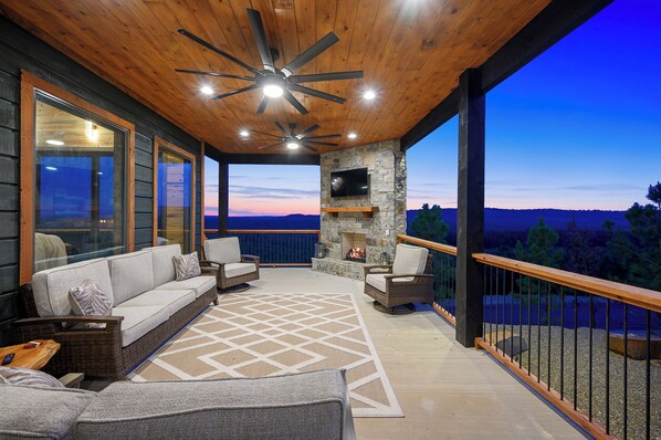 A covered outdoor seating area with a stone fireplace, wicker furniture, and a view of the landscape.
