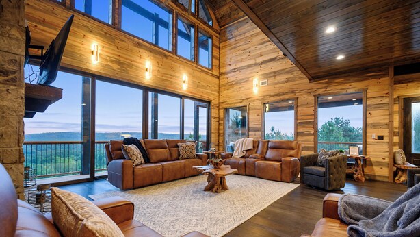 Ein geräumiges Wohnzimmer mit Ledersofas, einem großen Holztisch und großen Fenstern mit Blick ins Freie.