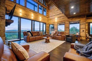 A spacious living room with leather sofas, a large wooden coffee table, and large windows offering a view of the outdoors.