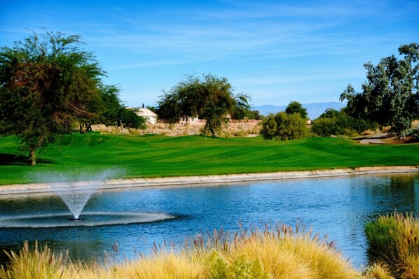 A golf course with a pond, trees, and a building in the background.