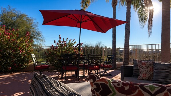 Un patio al aire libre con un paraguas rojo, una mesa, sillas y un sofá con cojines estampados.