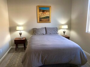 A bedroom with a bed, two bedside tables with lamps, a rug, and a painting on the wall.