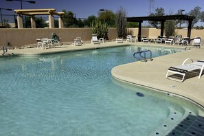 Una piscina cristalina con sillones de descanso y una pérgola.