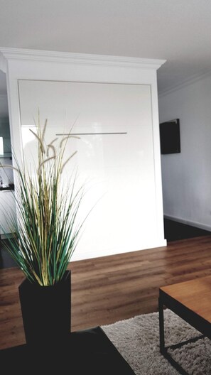 Ein modernes Wohnzimmer mit Holzboden, einer schwarzen Couch, einem kleinen Tisch und einer Topfpflanze.